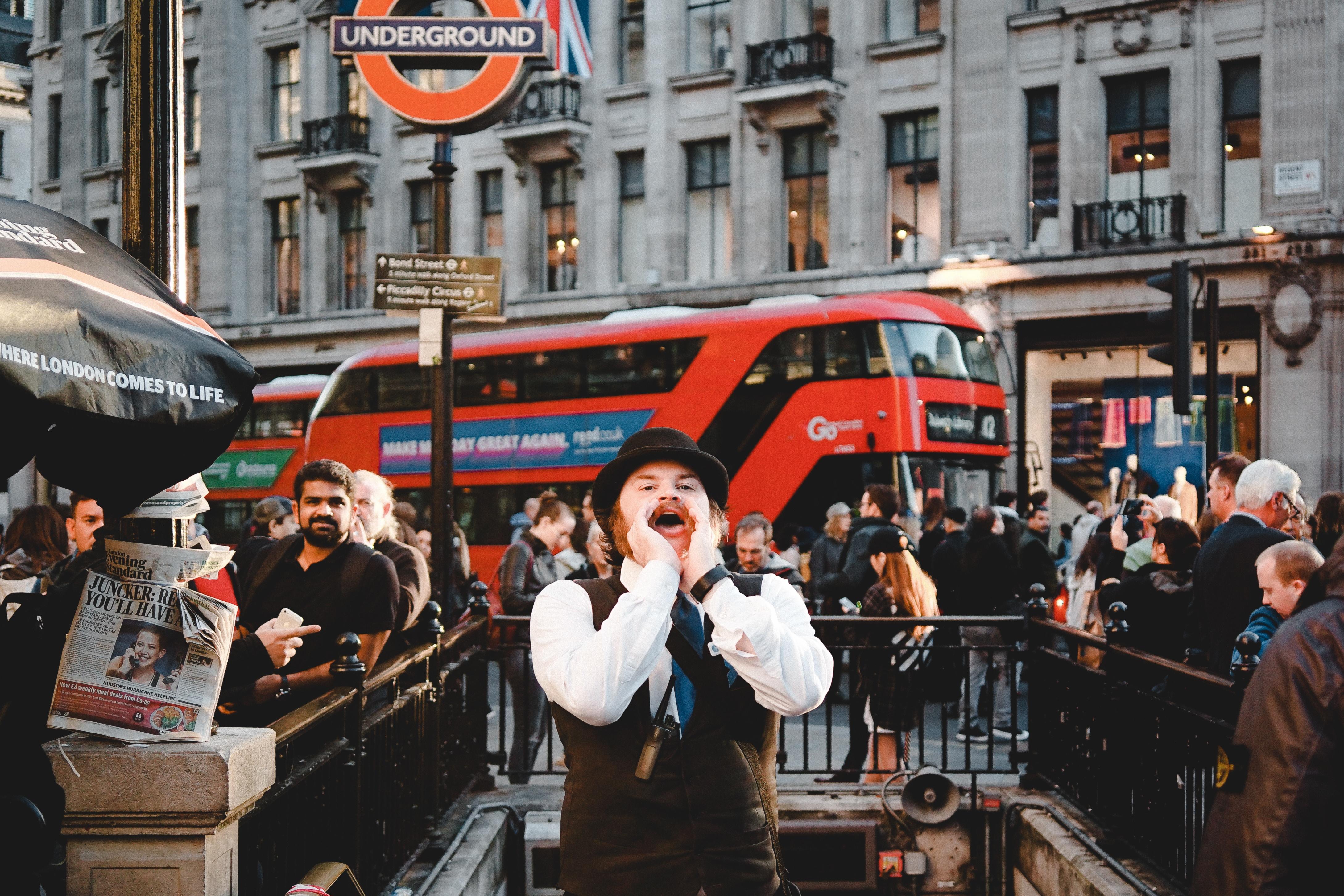 Man cupping his hands around his mouth and shouting at crowds by a London Underground Station