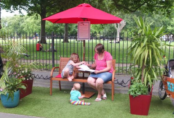 Woman and two children read on a bench in a parklet in Hackney