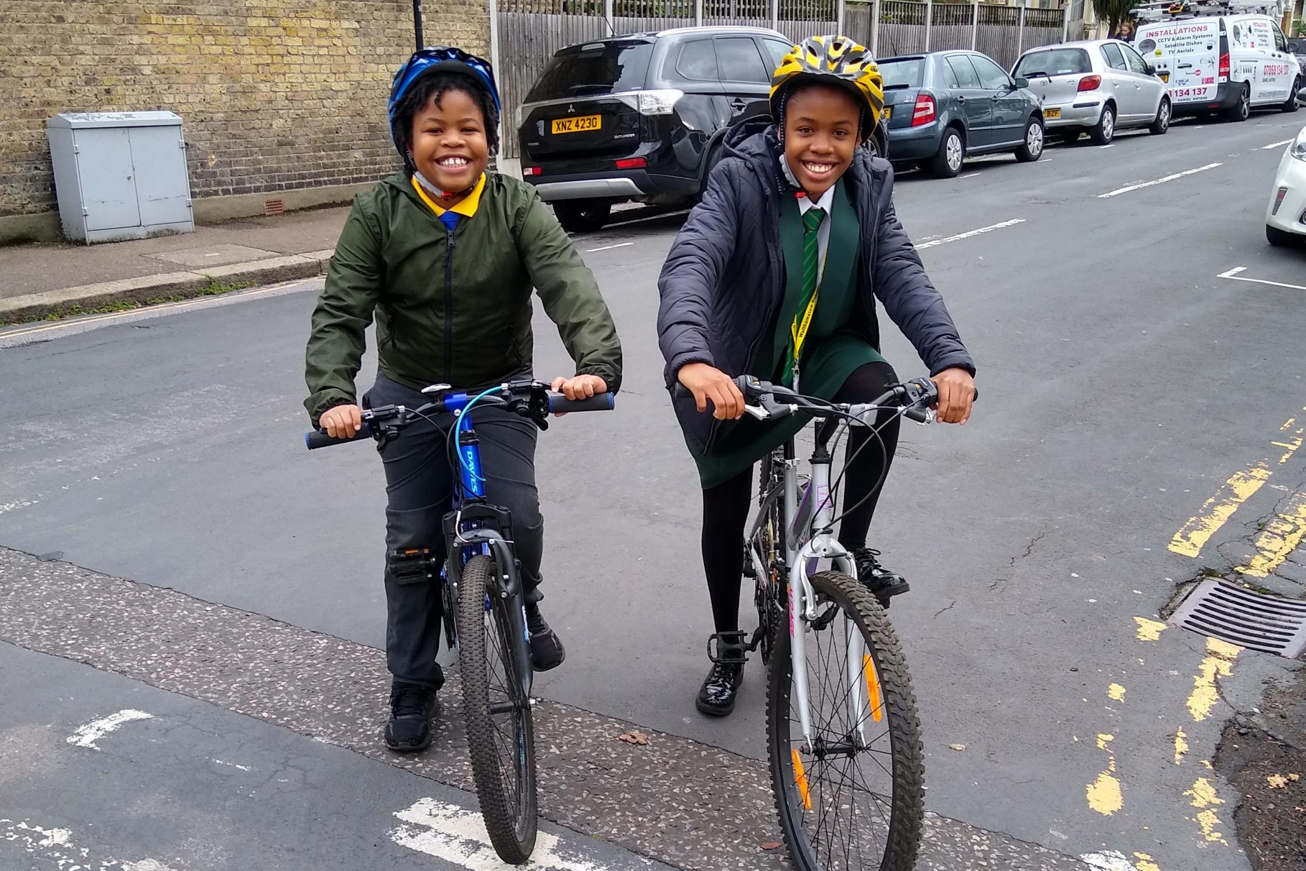 Smiling kids on bikes with helmets waiting at a junction